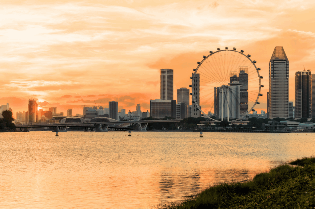Singapore skyline at sunset with the Singapore Flyer and Marina Bay Sands silhouetted against a warm orange sky; reflections shimmer across the water, blending architectural grandeur with natural serenity—capturing the city’s iconic landmarks bathed in golden hour light.