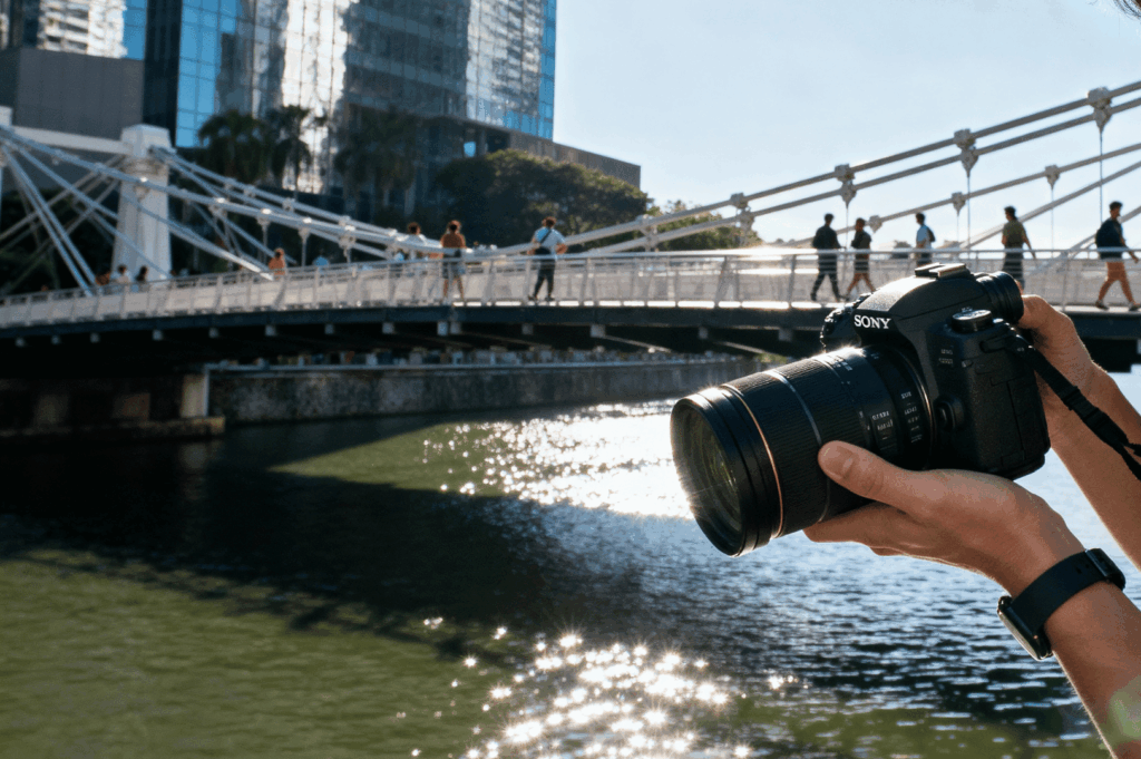 Photographer holding a camera at midday with a bridge in the background, testing Sony Alpha in harsh light, Singapore feature article