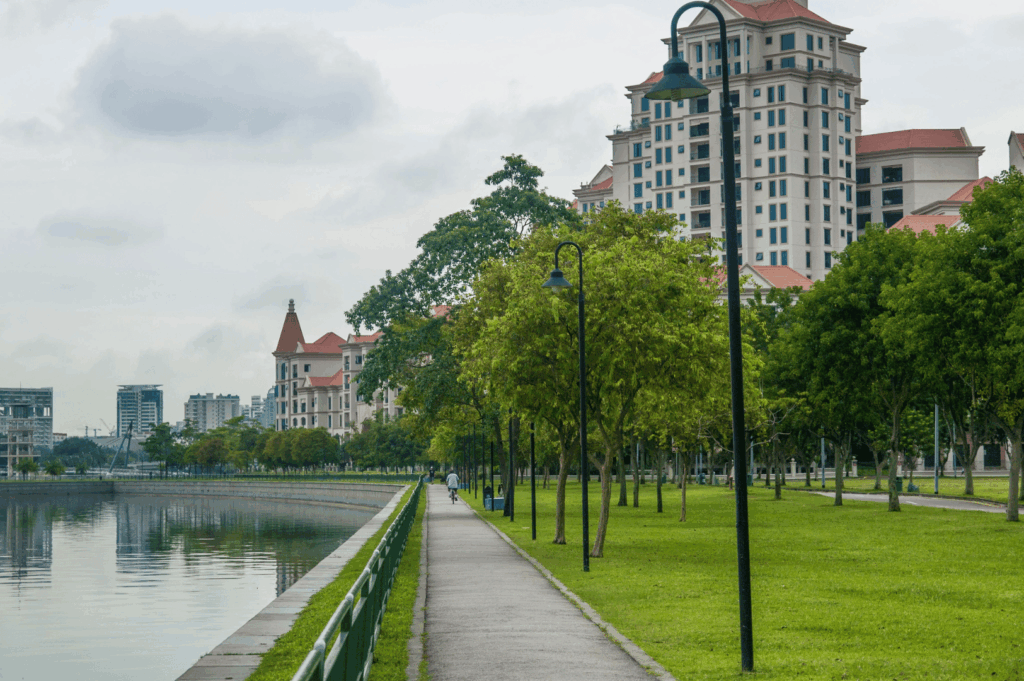 Serene riverside walkway in Singapore with tree-lined paths and red-roofed buildings, offering a peaceful, lesser-known spot for urban photography away from the tourist crowds.