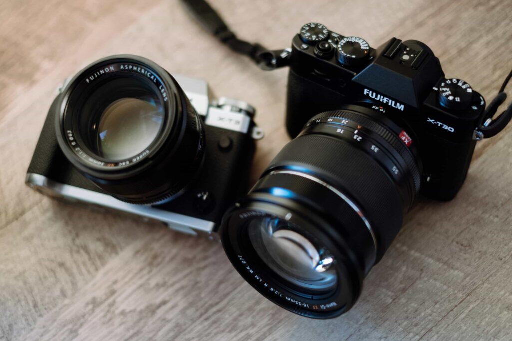 An image of two types of Fujifilm cameras displayed on a textured wooden table.