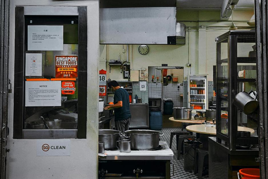 A photo of a Hawker chef preparing the for the day's meals inside his kitchen surrounded by pots and food.