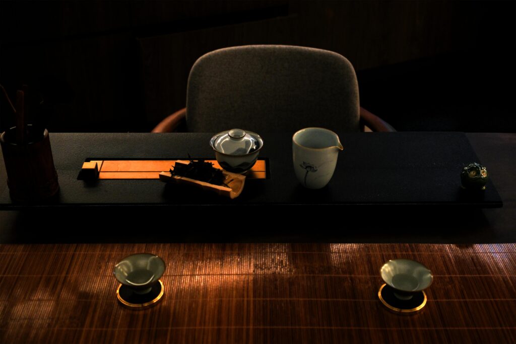 An elegant Gongfu tea set is meticulously arranged on a dark stone tea tray and a textured bamboo mat. The low-light setting highlights the delicate ceramic cups, a covered gaiwan, and a small tea pet, creating a serene and focused atmosphere.