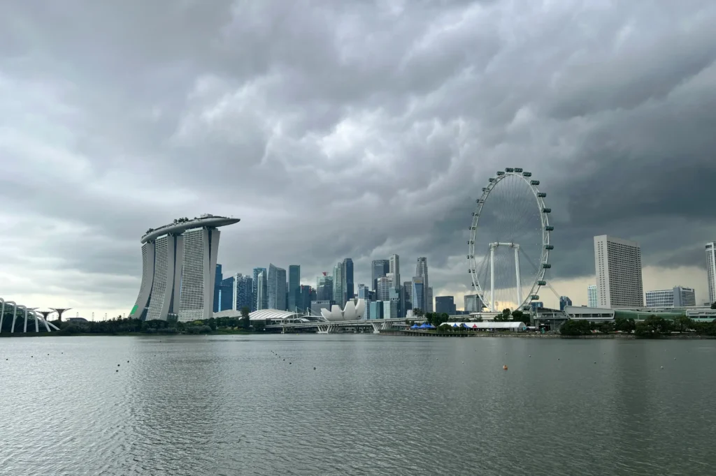 A wide shot captures the Singapore skyline under a heavy, overcast sky filled with dramatic grey storm clouds. The iconic Marina Bay Sands and Singapore Flyer stand prominently along the waterfront, reflecting the city's modern architectural style.
