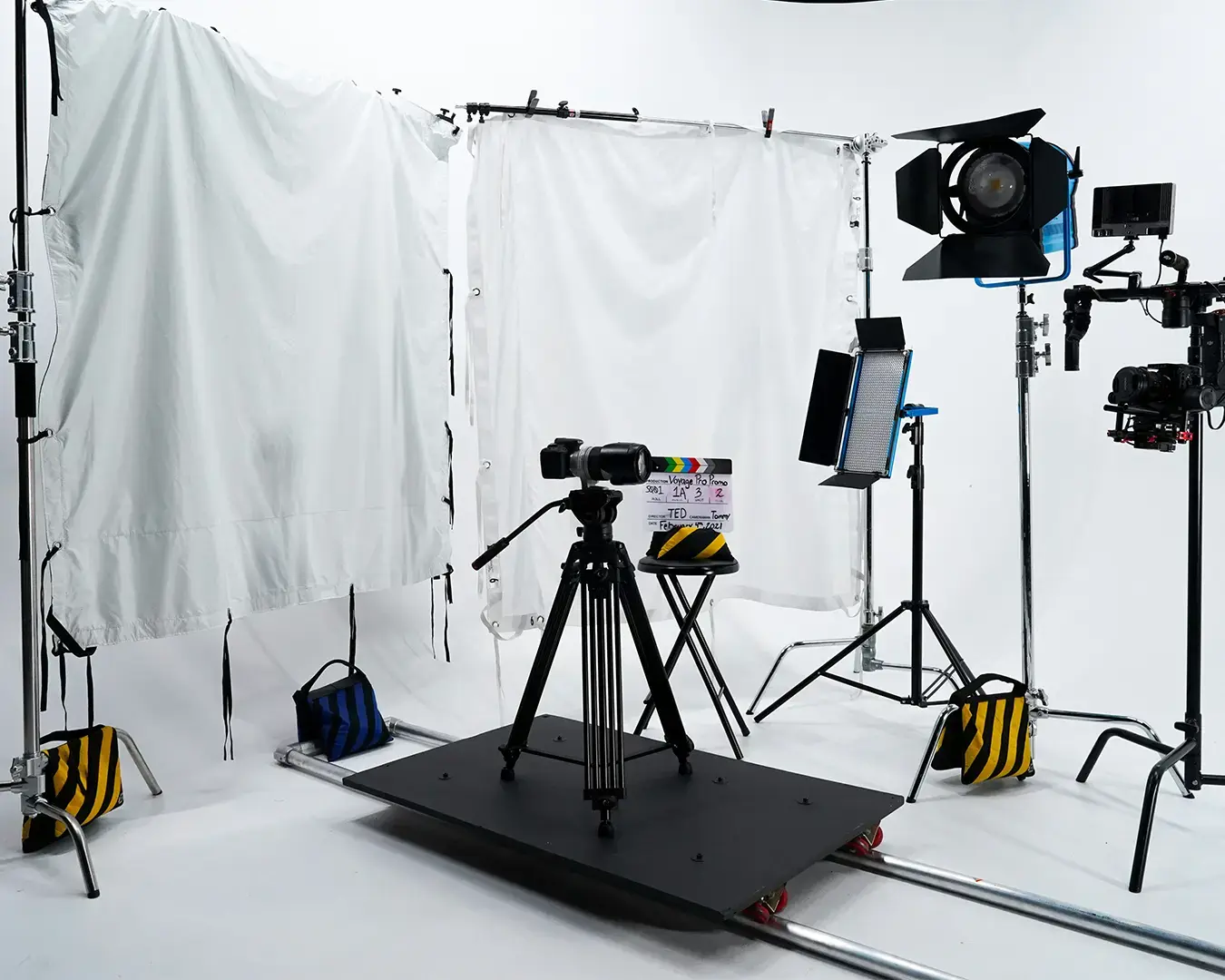 Film studio setup with cameras on tripods, bright lights, and white diffusion screens. Clapperboard and sandbags add to the professional ambiance.