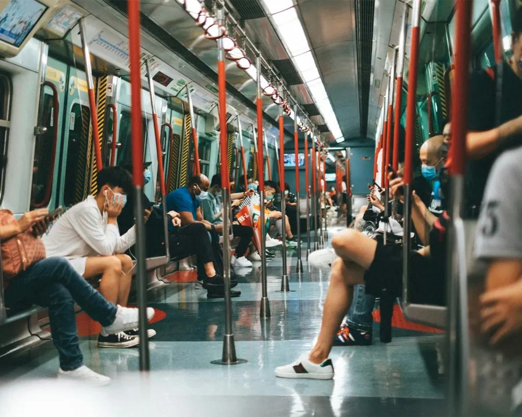 People sitting in a subway train, engrossed in their phones. The atmosphere is calm, with bright lights and red handrails lining the carriage.