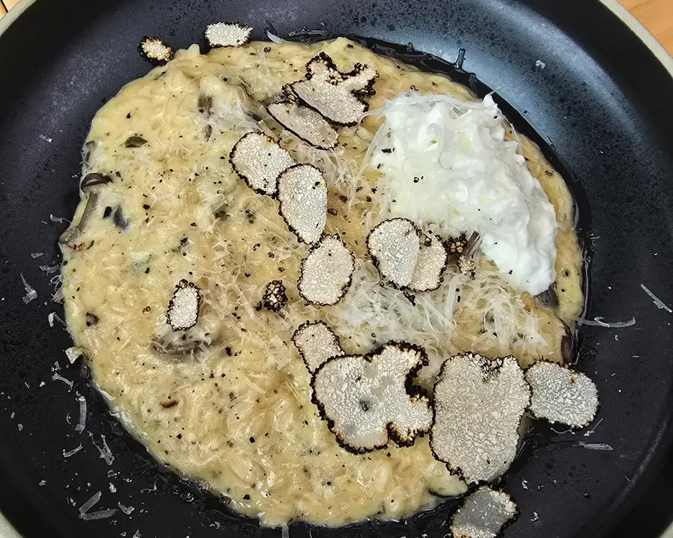 Creamy risotto topped with shaved truffles, grated cheese, and a dollop of cream on a dark plate, creating an elegant, rich presentation.