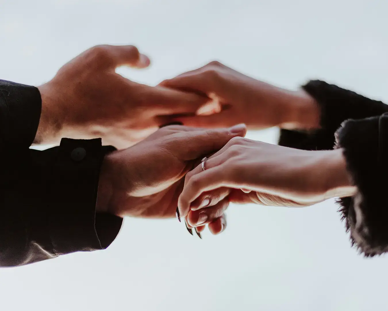 Couples holding hands in front of a bright blue sky, representing togetherness and connection.