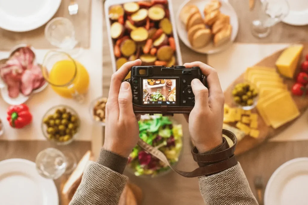 Hands holding a camera over a table of assorted food and drinks.