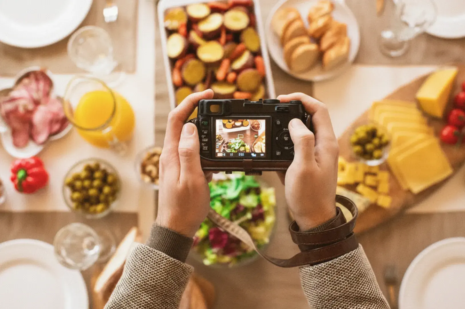 Hands holding a camera over a table of assorted food and drinks.