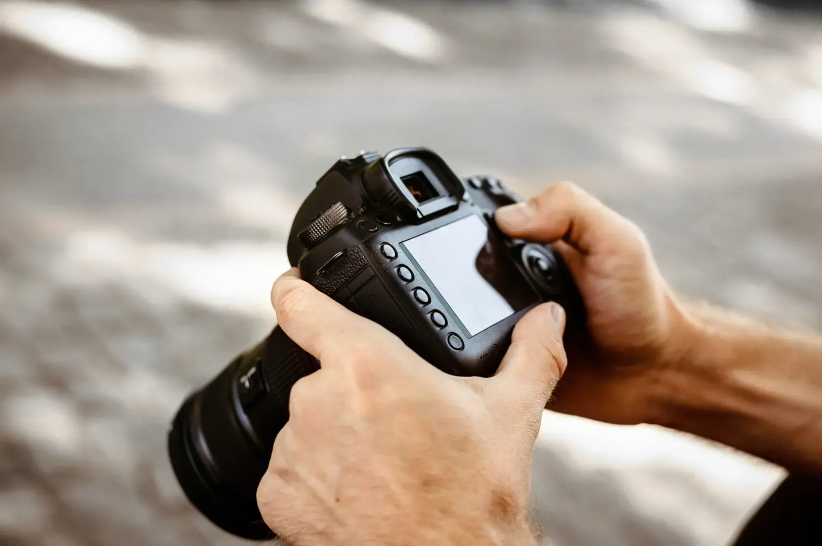 A person is holding a black DSLR camera with both hands, with fingers on the buttons and lens.