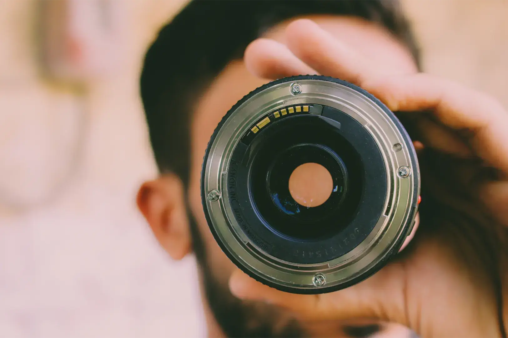 A person holds a camera lens up to their eye, looking through it.