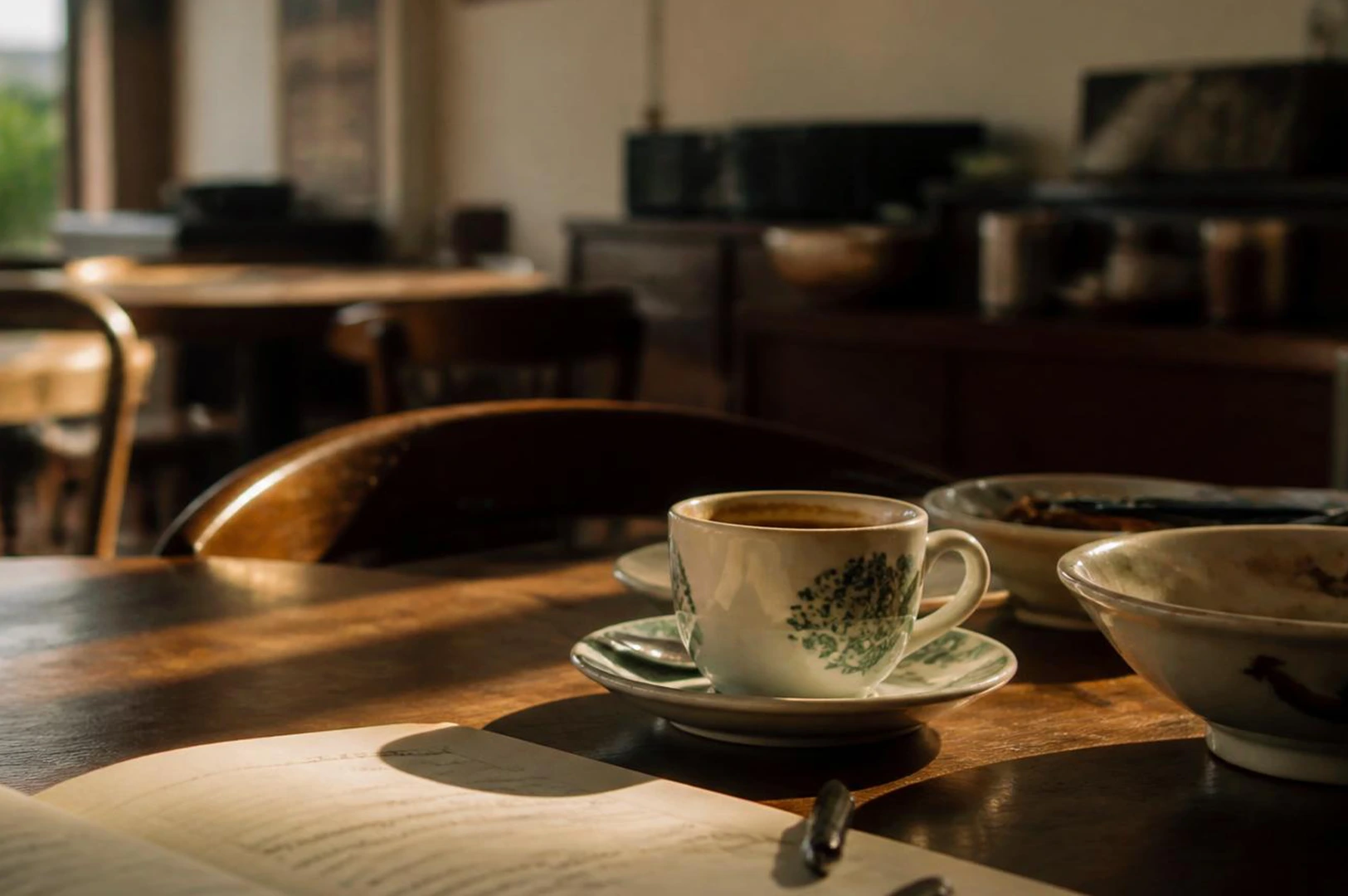 Coffee cup and open book on wooden table with afternoon light.