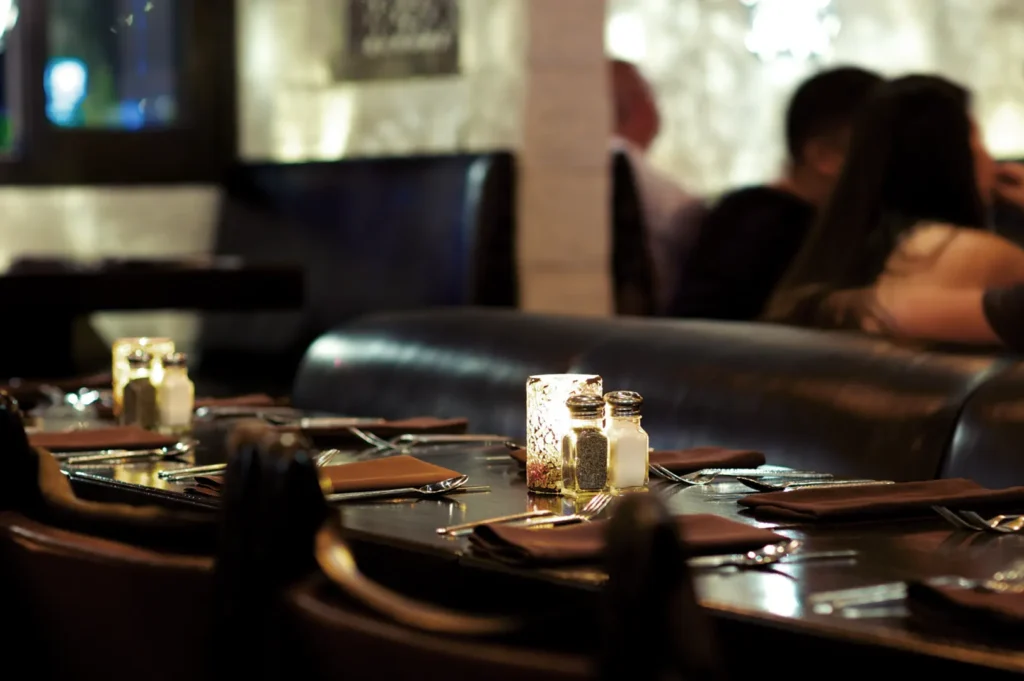 A dimly lit restaurant dining area with tables set for dinner, featuring leather booths and candles on the tables.