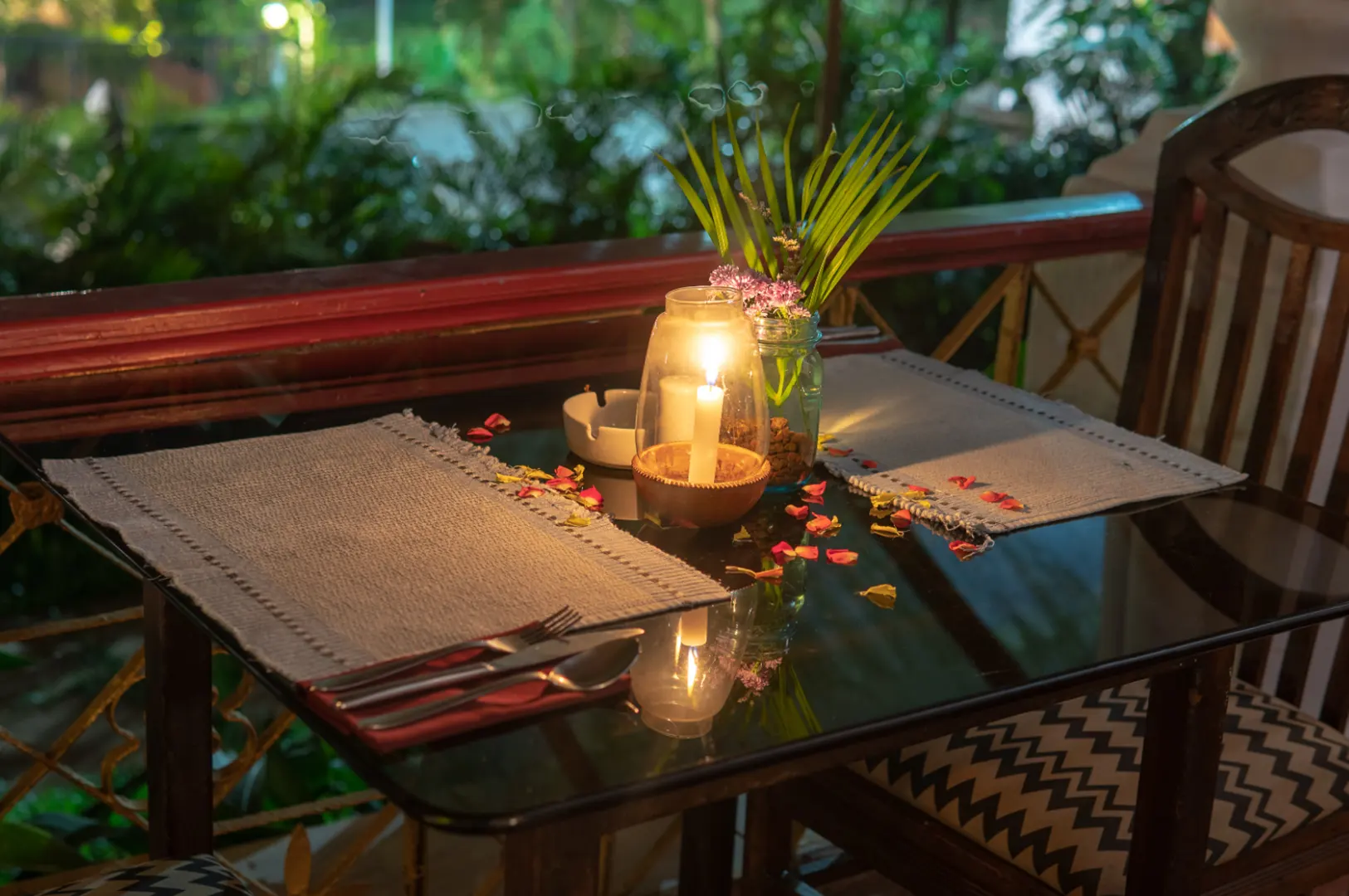 A table set for two with candles and rose petals, on a balcony at night.