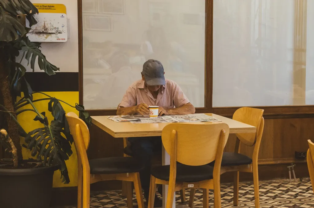 Senior man reading a newspaper at a café table.