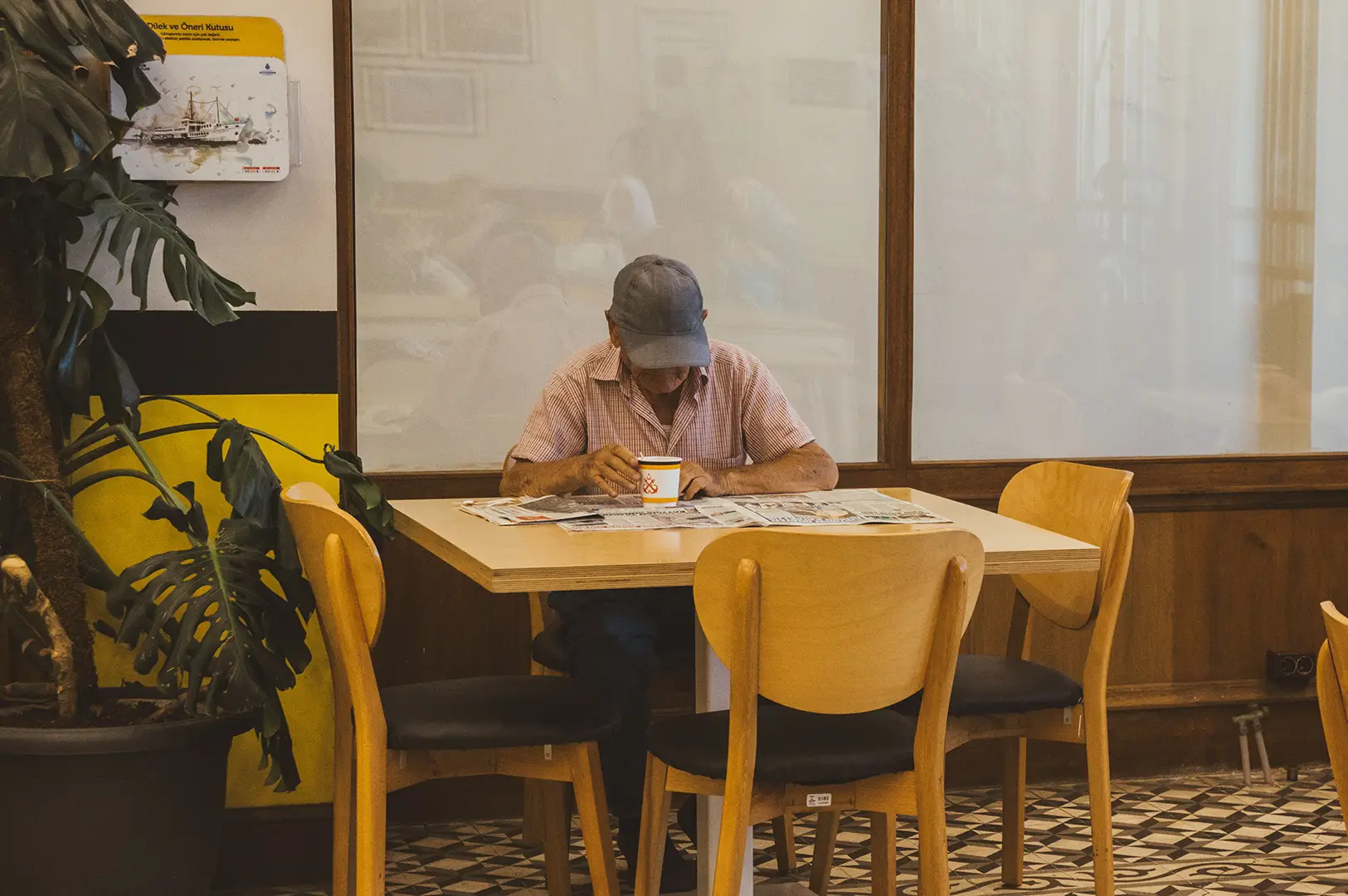 Senior man reading a newspaper at a café table.