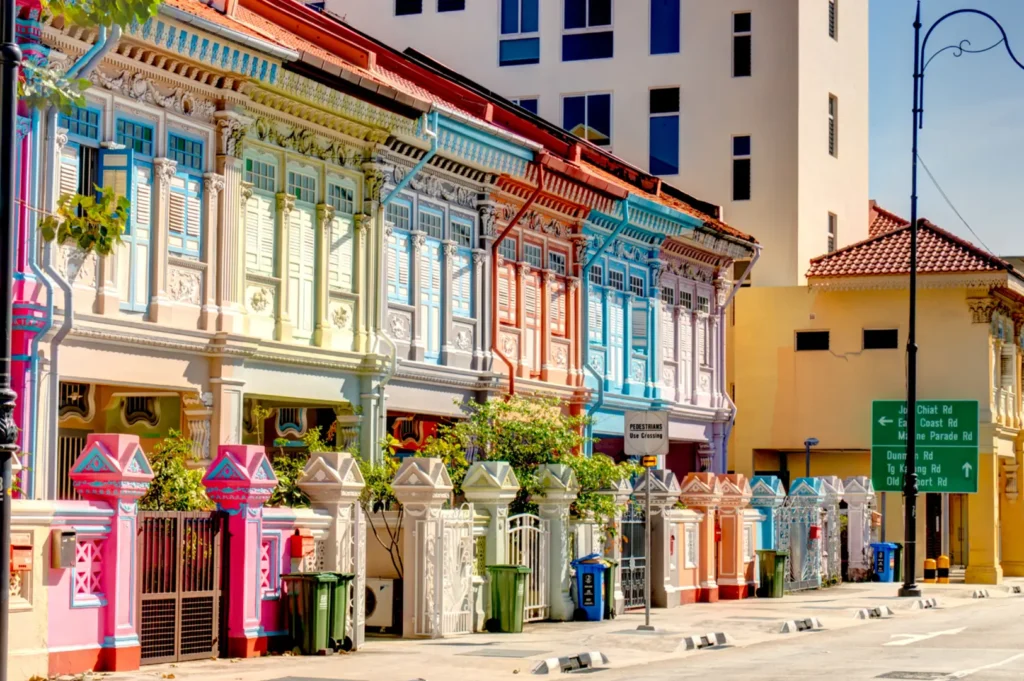 Colorful row of colonial-style shopfronts with balconies and painted facades lining a quiet street, with streetlights and green signs along the sidewalk.