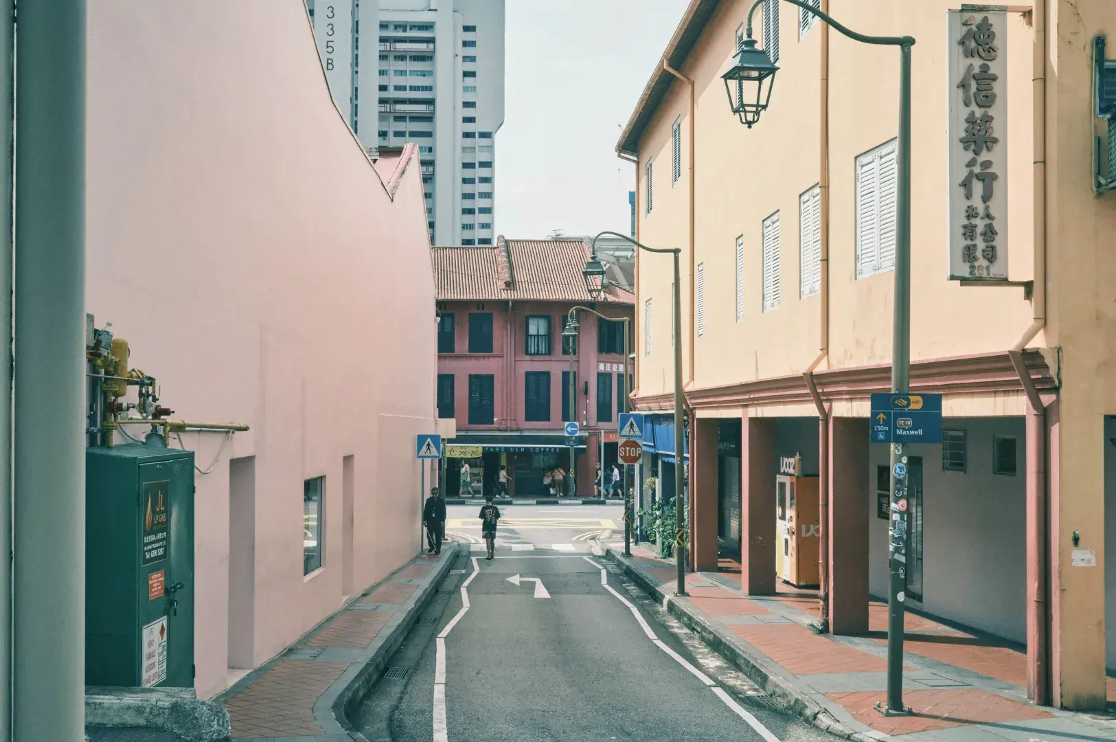 A narrow street lined with colorful buildings, including a pink building on the left and orange and red buildings on the right. A modern skyscraper is visible in the background.