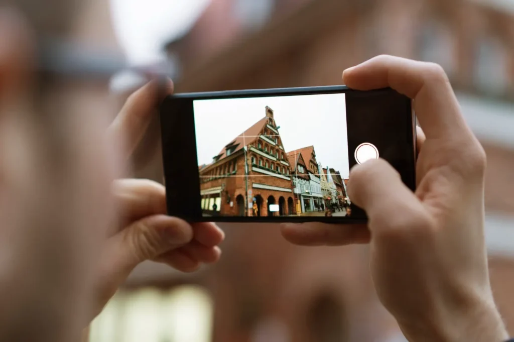 A person holds a smartphone horizontally, photographing a historic building street scene on the screen.
