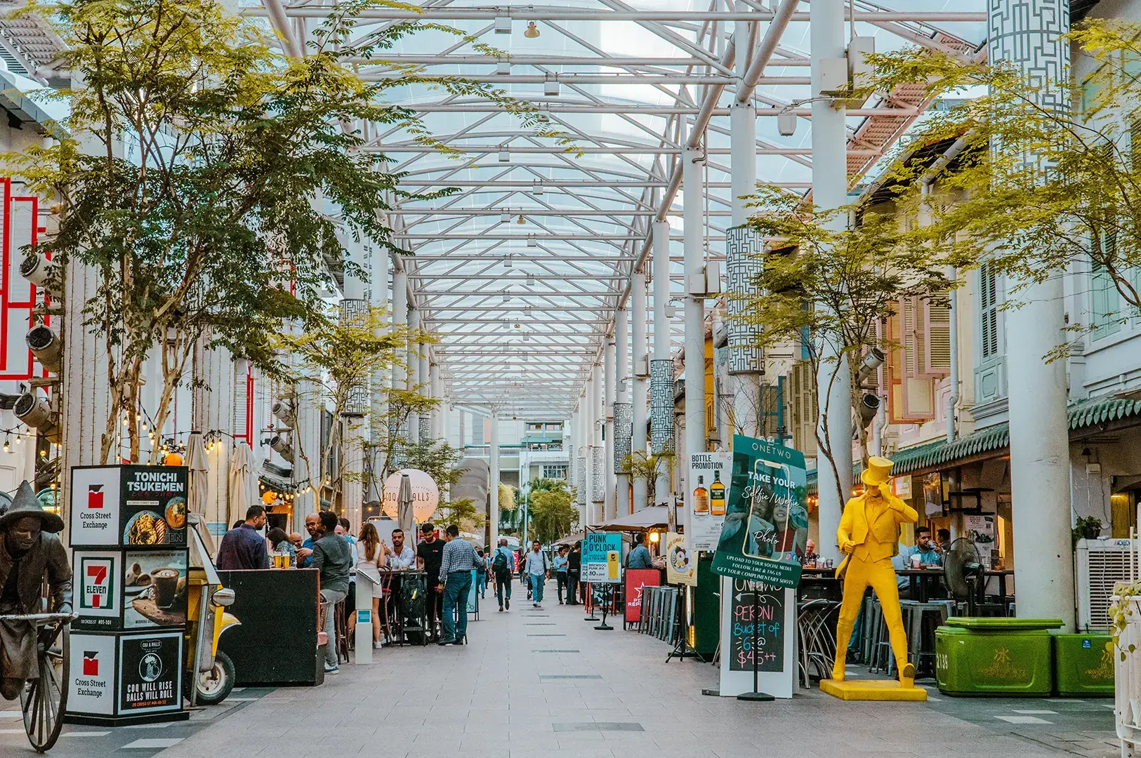 A covered street dining lane with people sitting at food stalls and café tables.