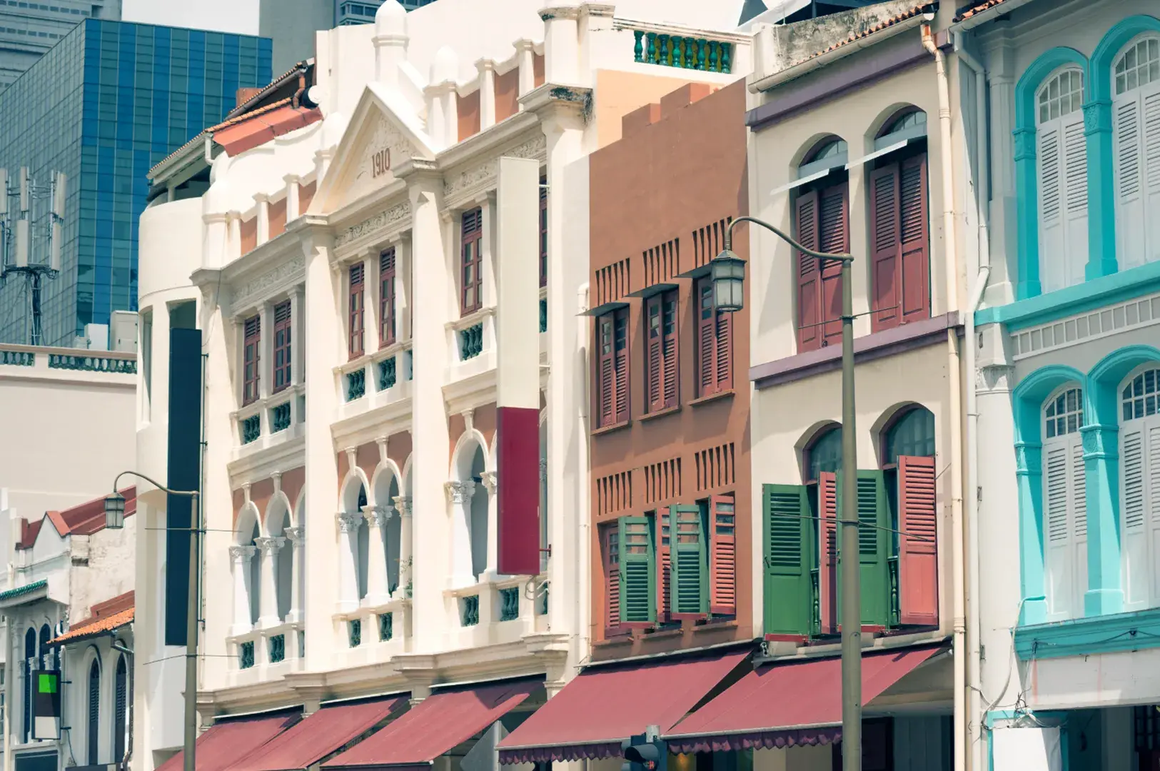 Row of colorful heritage buildings with ornate facades and shutters, contrasted by a modern skyscraper in the background.