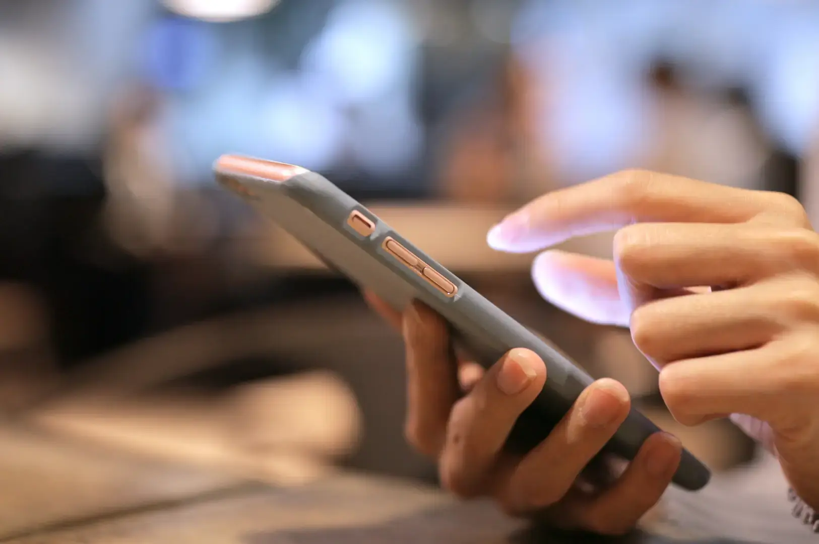 A person holding a smartphone and tapping the screen with a finger, with a blurred background of people and seats.