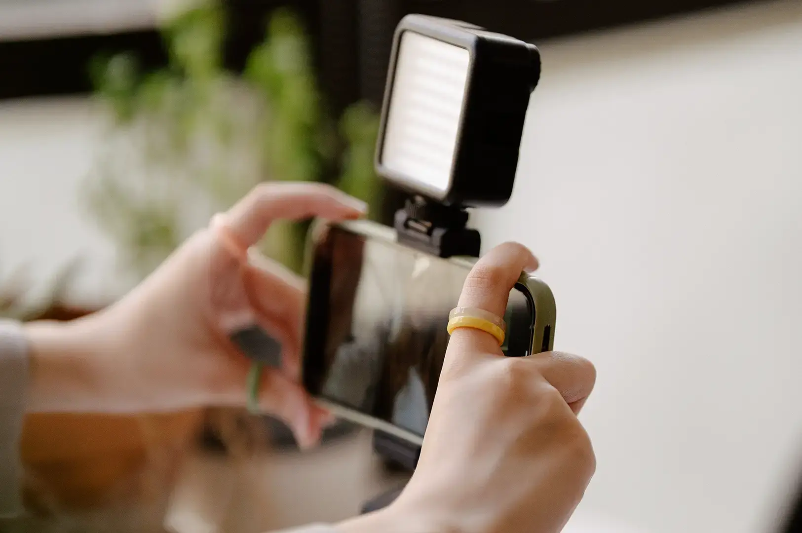 Hands hold a smartphone with an attached LED light panel.