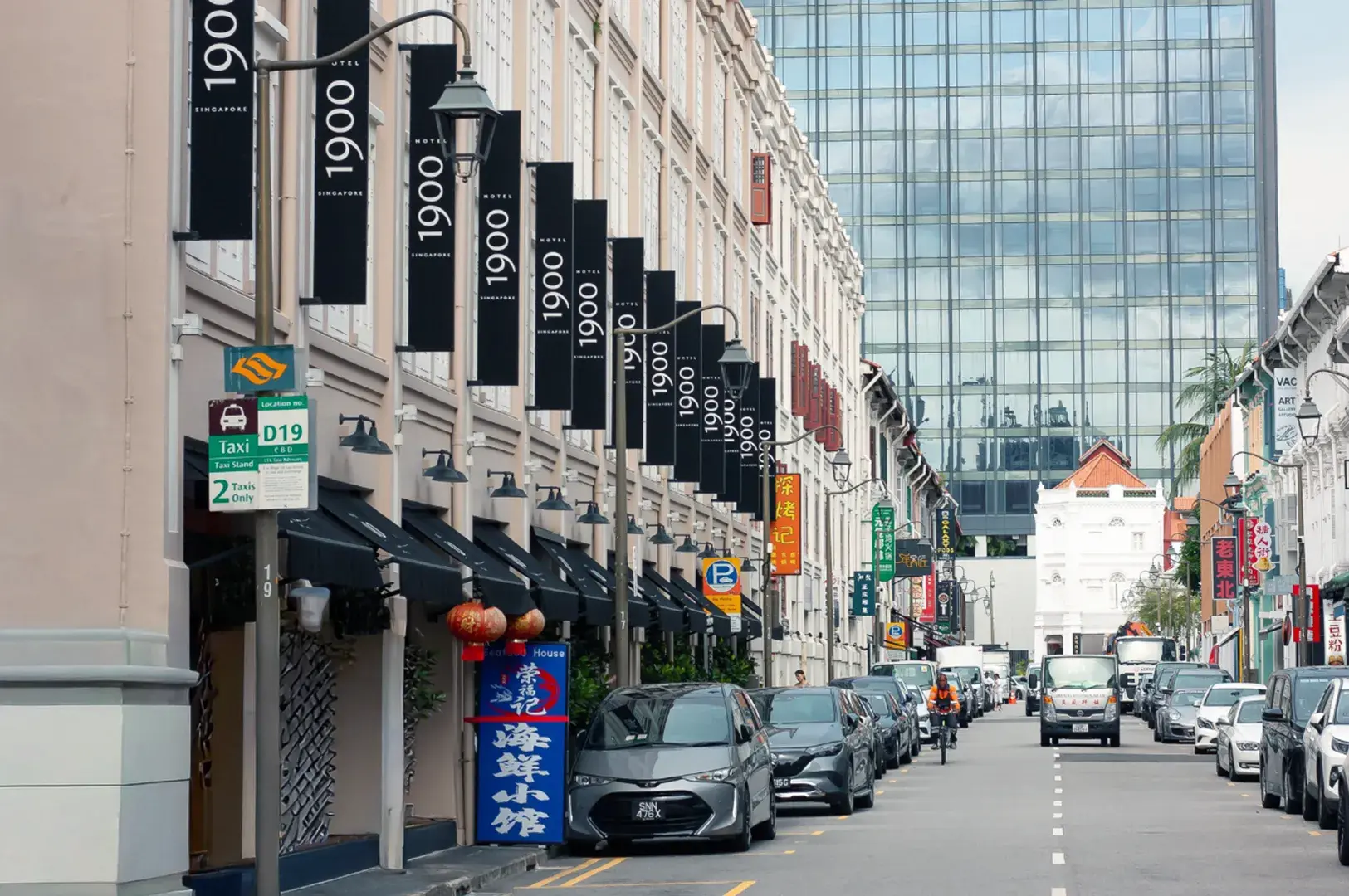 A street lined with traditional buildings and modern skyscrapers, with cars parked along the side and signs in Chinese and English.