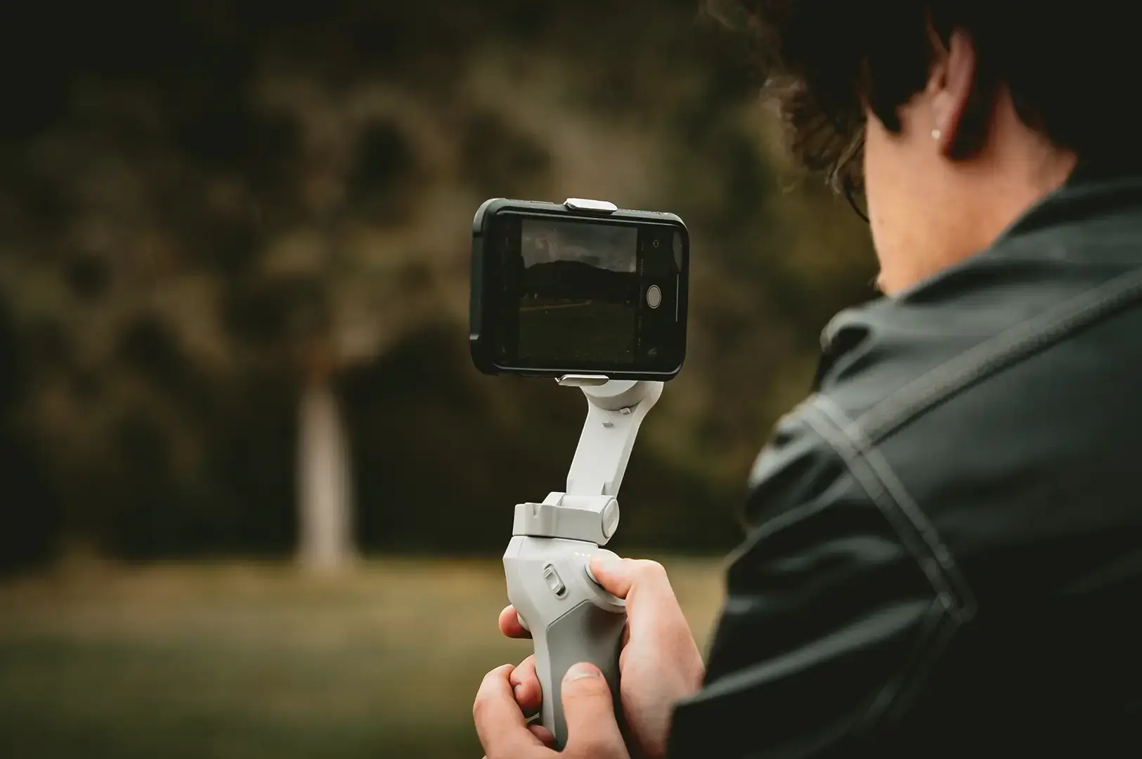 A person holds a smartphone mounted on a handheld gimbal outdoors.