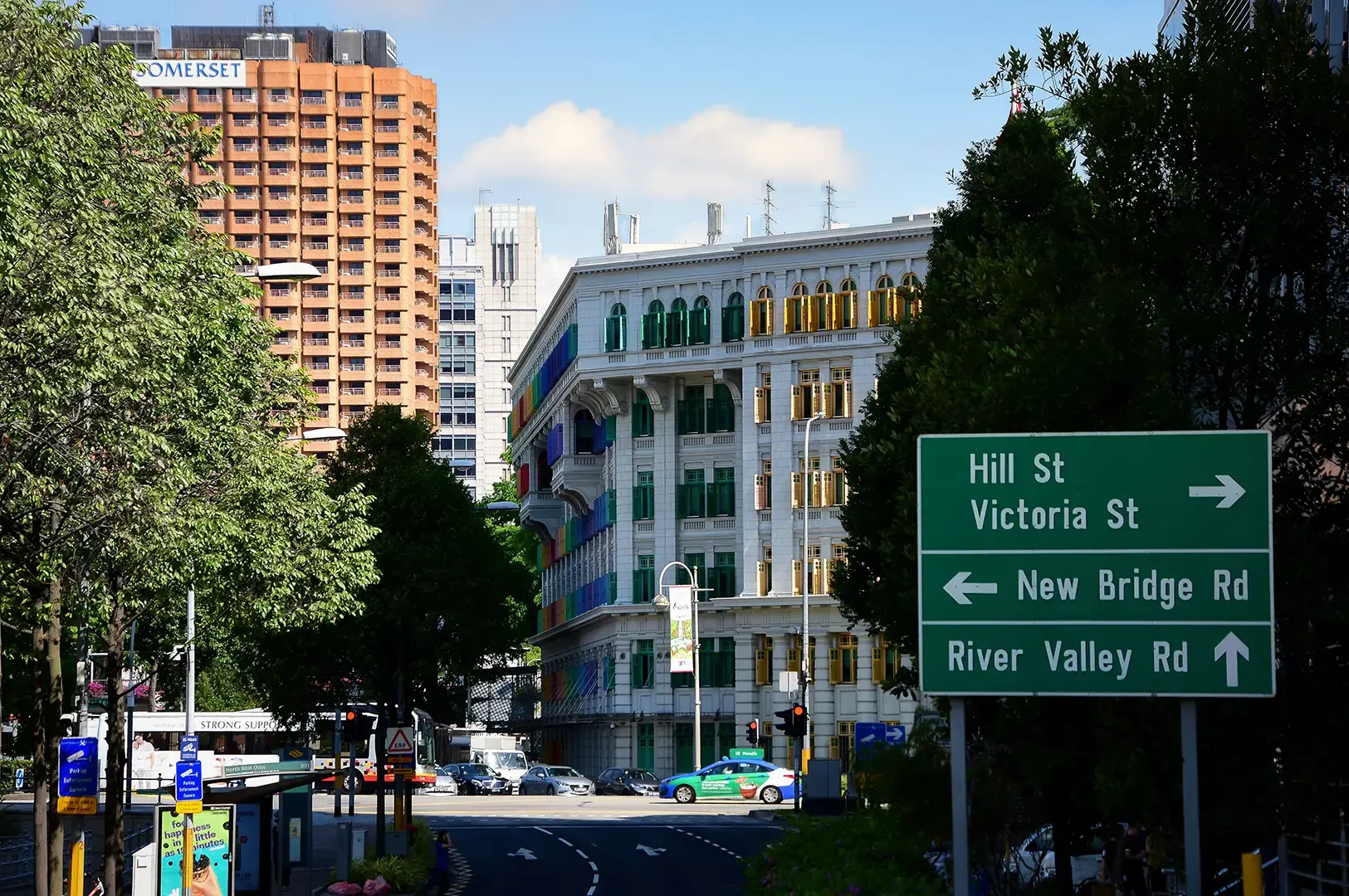 A street view with the colourful old Hill Street Police Station beside road signs and trees.