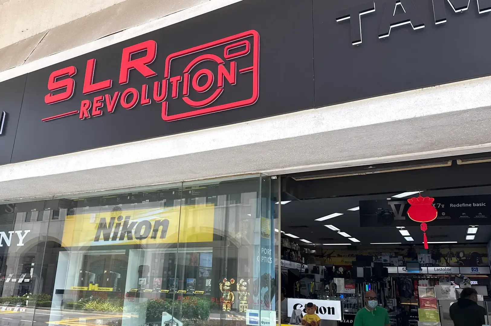 SLR Revolution camera shop entrance with red signage, Nikon and Canon displays, and customers inside.