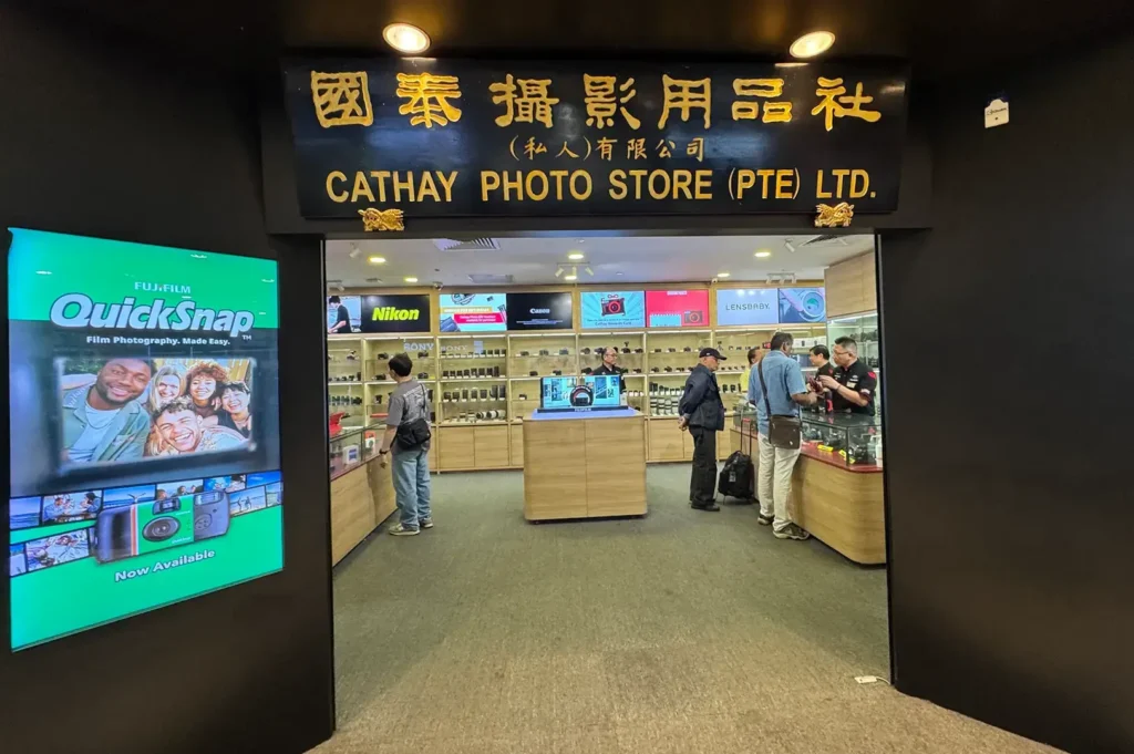 Cathay Photo Store entrance with Chinese signage, camera displays, product counters, and customers browsing inside.