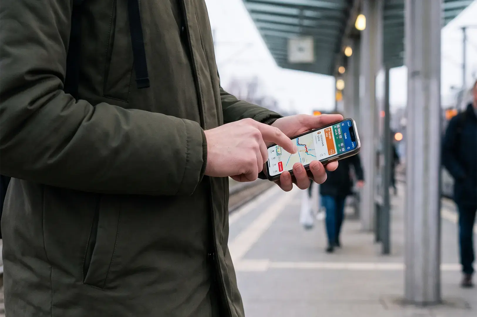 Close-up of a person using a navigation map app on a smartphone while waiting at a train station.