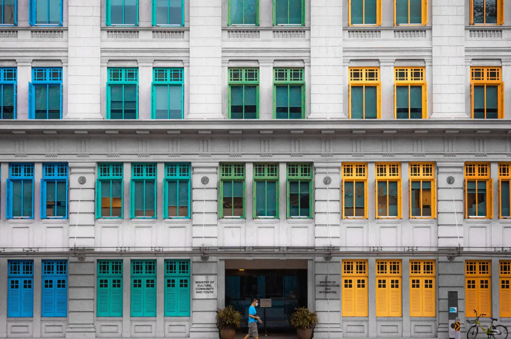 Hill Street heritage building with rows of blue, turquoise, green, and yellow windows and doors, with a person standing near the entrance.