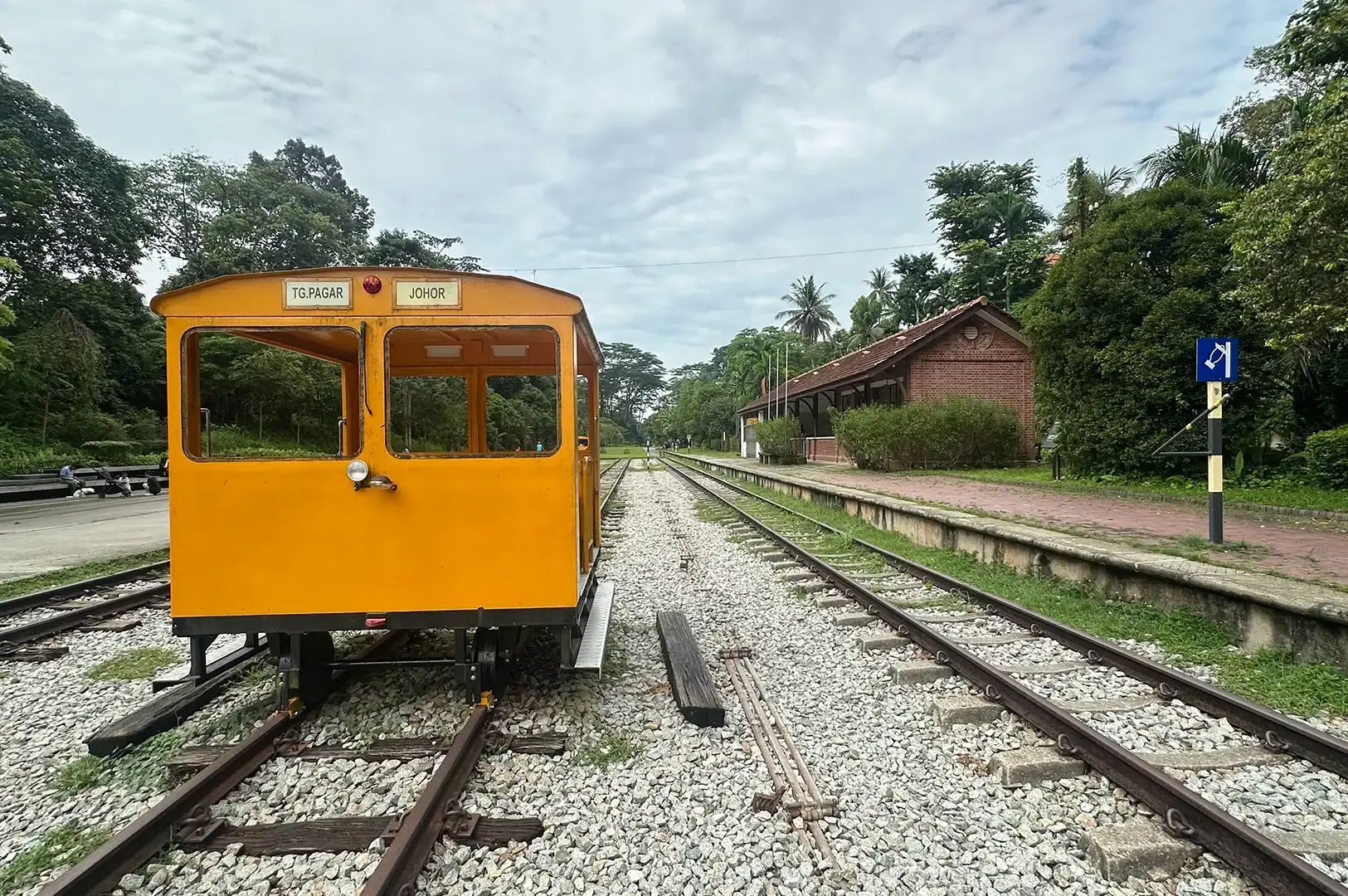 Yellow railway inspection vehicle on tracks beside the former Bukit Timah Railway Station, surrounded by trees and greenery.